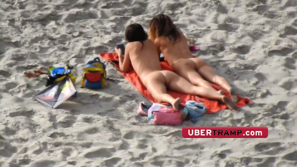 Naked girl with spread legs enjoys the nudist beach with her best friend